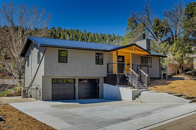 single story home with a garage, driveway, metal roof, and stucco siding