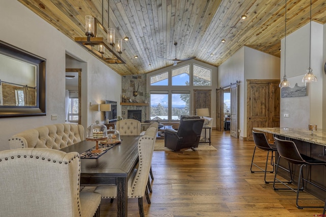 dining area featuring a fireplace, wood-type flooring, high vaulted ceiling, wooden ceiling, and a barn door