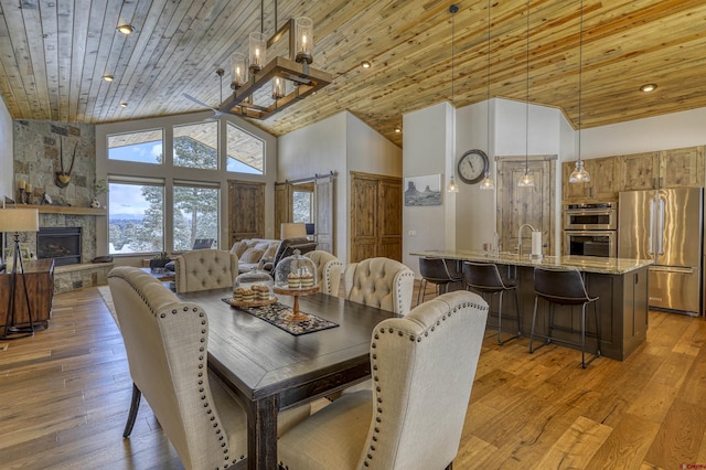 dining area featuring wood ceiling, wood-type flooring, a stone fireplace, and high vaulted ceiling