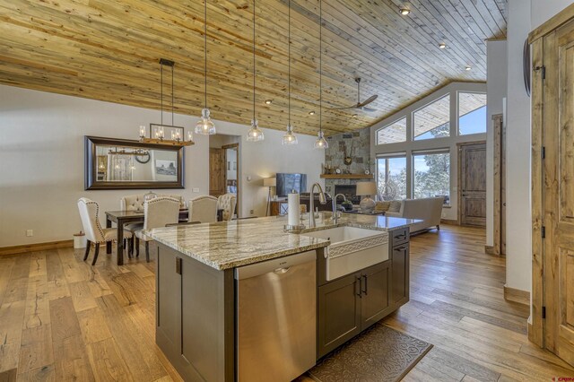 kitchen with sink, hanging light fixtures, light stone counters, a center island with sink, and stainless steel dishwasher