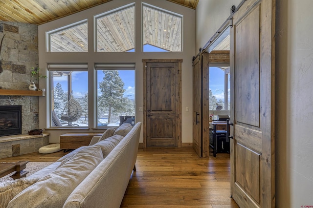 living room featuring wood ceiling, a towering ceiling, a fireplace, wood-type flooring, and a barn door