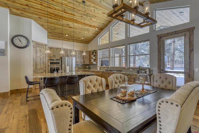 dining space featuring light wood-type flooring, an inviting chandelier, wooden ceiling, and high vaulted ceiling