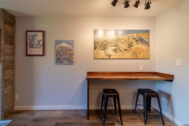 bar featuring rail lighting, baseboards, and dark wood-type flooring