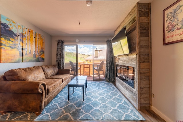 living room featuring a textured ceiling, a fireplace, wood finished floors, and baseboards