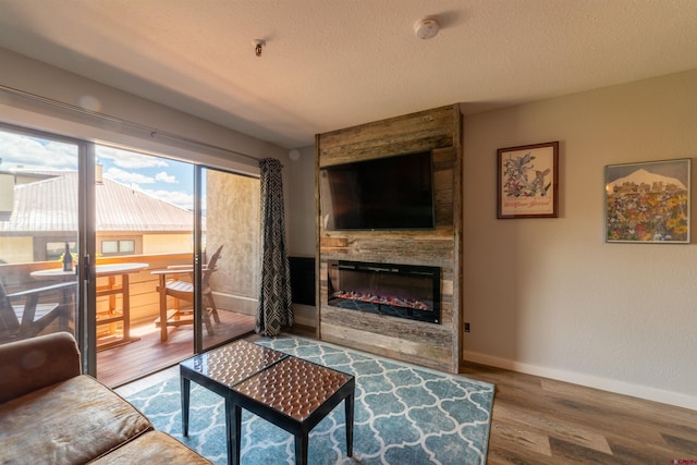 living area with a large fireplace, a textured ceiling, baseboards, and wood finished floors