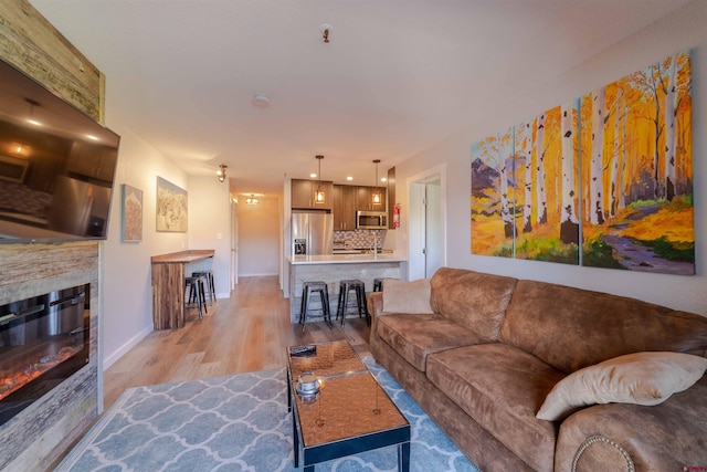 living room featuring light wood-type flooring, a glass covered fireplace, and baseboards