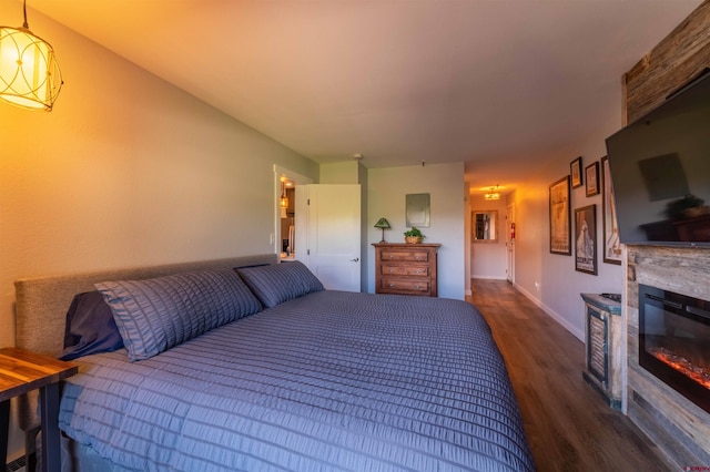 bedroom with a glass covered fireplace, dark wood finished floors, and baseboards