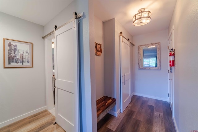 hallway with a barn door, wood finished floors, and baseboards