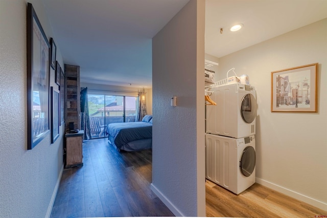 laundry room with laundry area, baseboards, stacked washing maching and dryer, and wood finished floors