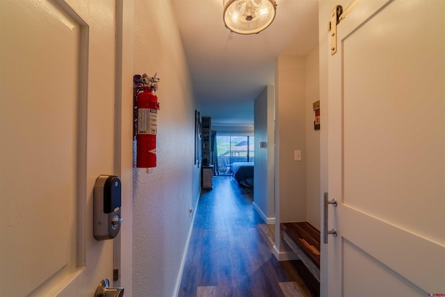 corridor with a barn door, dark wood finished floors, and baseboards