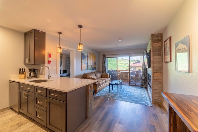 kitchen featuring dishwasher, open floor plan, a peninsula, light countertops, and a sink