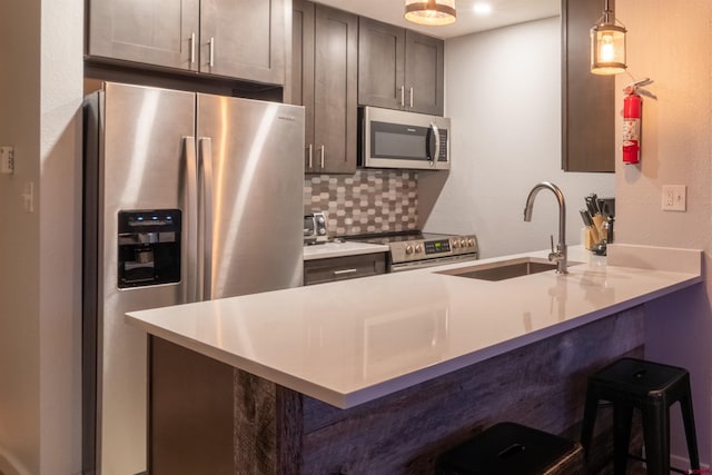 kitchen featuring stainless steel appliances, light countertops, decorative light fixtures, and a kitchen bar