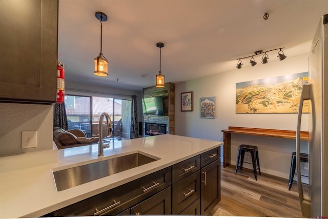 kitchen with dark brown cabinetry, light wood-style flooring, hanging light fixtures, light countertops, and a sink