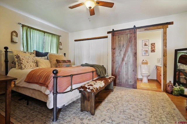 bedroom featuring wood-type flooring, a barn door, ceiling fan, and ensuite bath