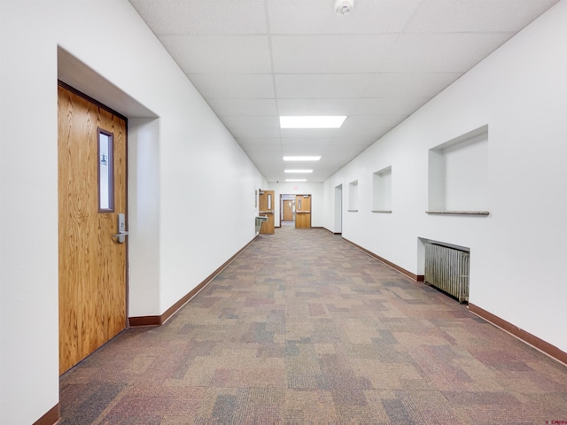 hall featuring radiator, carpet floors, and a drop ceiling