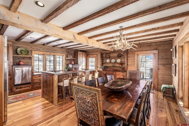 dining space with an inviting chandelier, wooden walls, light hardwood / wood-style flooring, and beamed ceiling