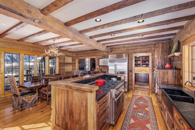 kitchen featuring beam ceiling, wooden walls, high quality appliances, a chandelier, and light wood-type flooring