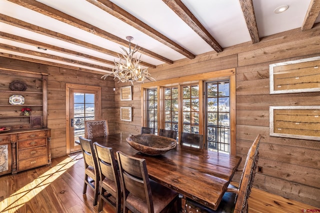 dining room featuring dark wood-type flooring, a notable chandelier, beam ceiling, and wood walls