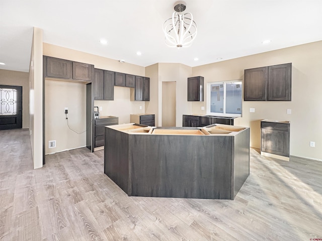 kitchen featuring dark brown cabinetry, an inviting chandelier, decorative light fixtures, a kitchen island, and light hardwood / wood-style floors