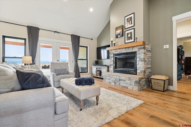 living room featuring high vaulted ceiling, a water view, a stone fireplace, french doors, and light wood-type flooring