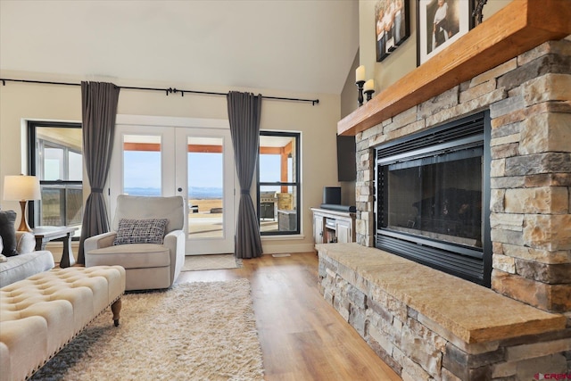 living room featuring a stone fireplace, high vaulted ceiling, french doors, and light wood-type flooring