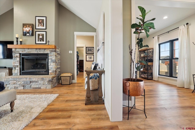 living room with vaulted ceiling, a stone fireplace, and light wood-type flooring