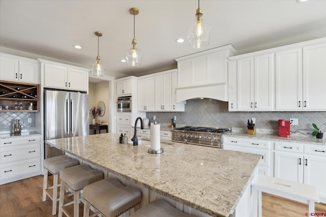 kitchen with appliances with stainless steel finishes, decorative light fixtures, a kitchen island with sink, and white cabinets