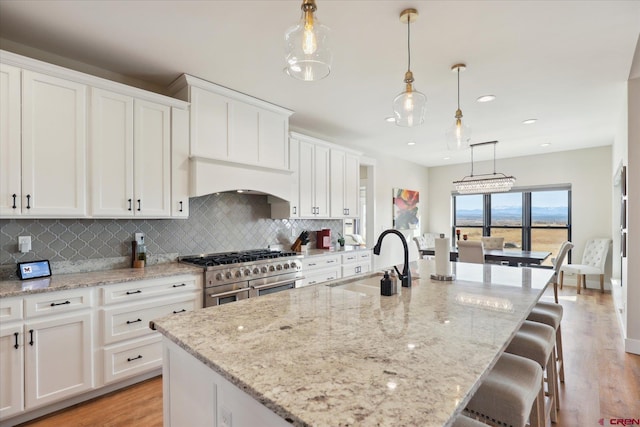 kitchen featuring sink, decorative light fixtures, a kitchen island with sink, and range with two ovens