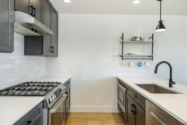 kitchen featuring decorative light fixtures, sink, backsplash, stainless steel appliances, and light hardwood / wood-style flooring