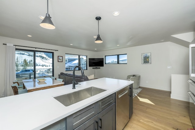 kitchen featuring sink, decorative light fixtures, stainless steel dishwasher, and light wood-type flooring