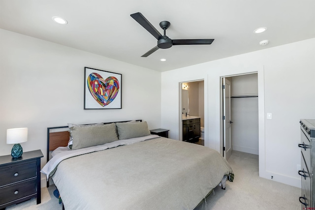 bedroom with ensuite bathroom, a spacious closet, light carpet, a closet, and ceiling fan