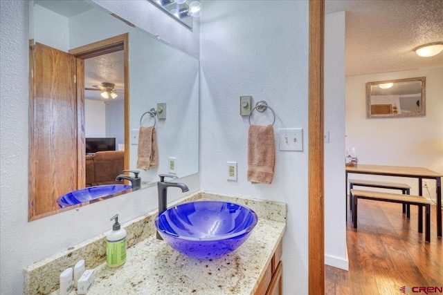 bathroom with hardwood / wood-style flooring, ceiling fan, vanity, and a textured ceiling