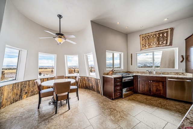 kitchen with sink, wood walls, ceiling fan, stainless steel appliances, and a high ceiling