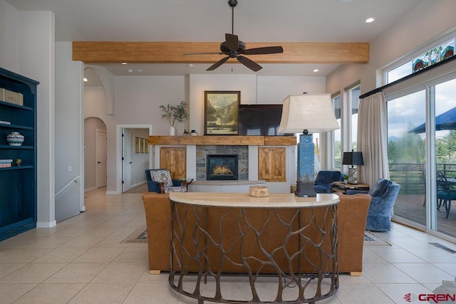 interior space featuring beam ceiling, light tile patterned floors, a stone fireplace, and ceiling fan