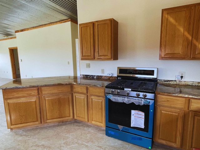 kitchen featuring stainless steel gas range, kitchen peninsula, and dark stone counters