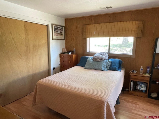 bedroom with wood walls, a closet, and light wood-type flooring