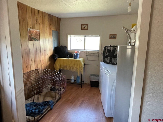 laundry room featuring wooden walls, hardwood / wood-style floors, a textured ceiling, and washer and clothes dryer