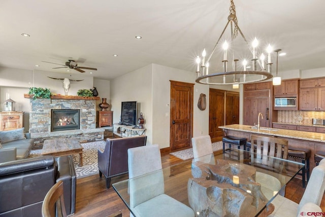 dining room with sink, ceiling fan with notable chandelier, a fireplace, and dark hardwood / wood-style floors