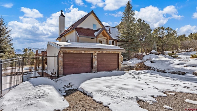 view of snowy exterior featuring stucco siding, driveway, stone siding, fence, and a chimney