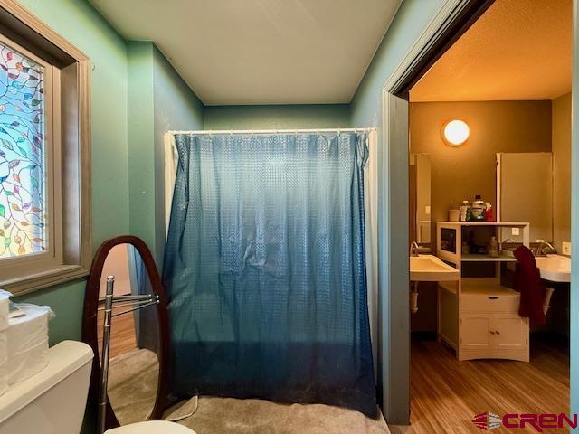 bathroom featuring wood-type flooring, shower / tub combo with curtain, and toilet