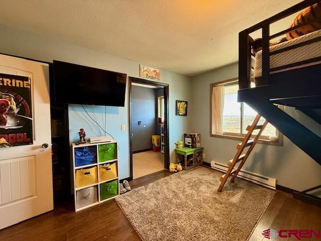 bedroom featuring a baseboard heating unit, dark wood-type flooring, and a textured ceiling