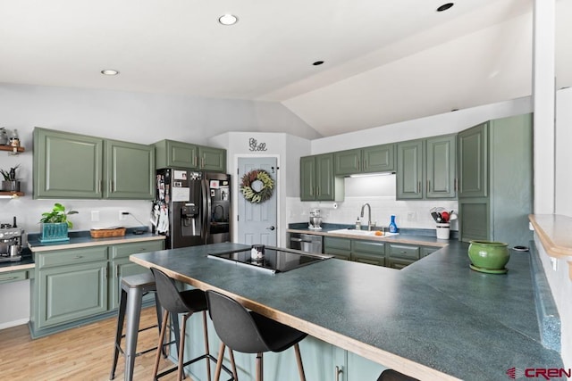 kitchen with lofted ceiling, a breakfast bar, sink, green cabinets, and stainless steel appliances