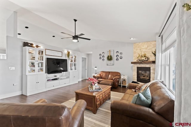 living room with wood-type flooring, a stone fireplace, lofted ceiling, and ceiling fan