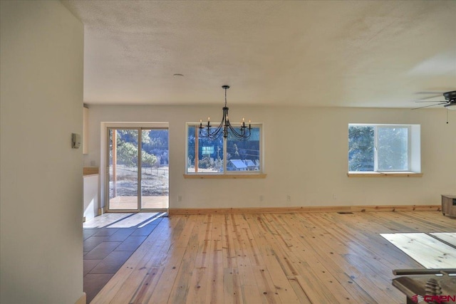 unfurnished dining area with ceiling fan with notable chandelier and light wood-type flooring