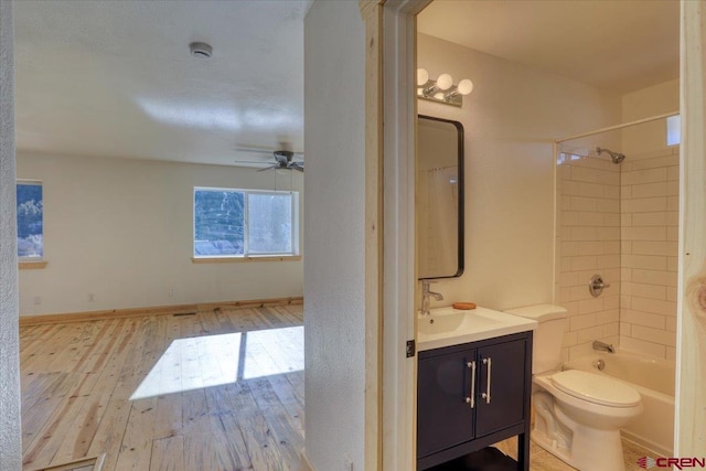 full bathroom with hardwood / wood-style flooring, vanity, tiled shower / bath combo, ceiling fan, and toilet