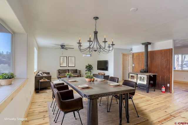 dining room with a wood stove, ceiling fan with notable chandelier, and light hardwood / wood-style floors