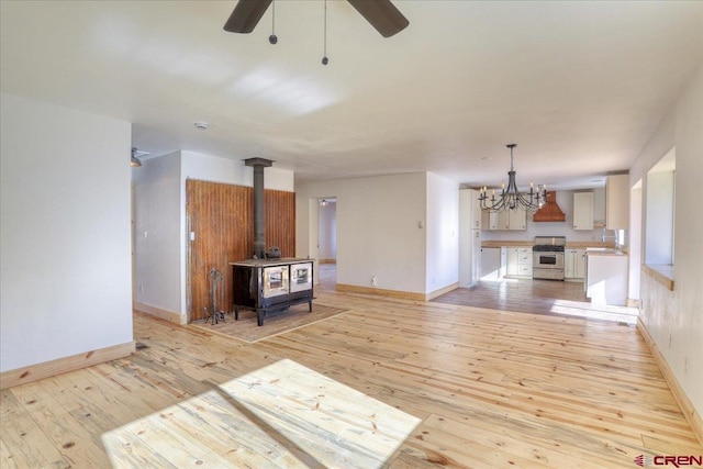 unfurnished living room with ceiling fan with notable chandelier, sink, light hardwood / wood-style floors, and a wood stove