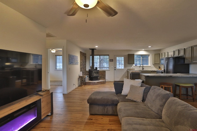 living room with hardwood / wood-style floors, sink, ceiling fan, and a wood stove