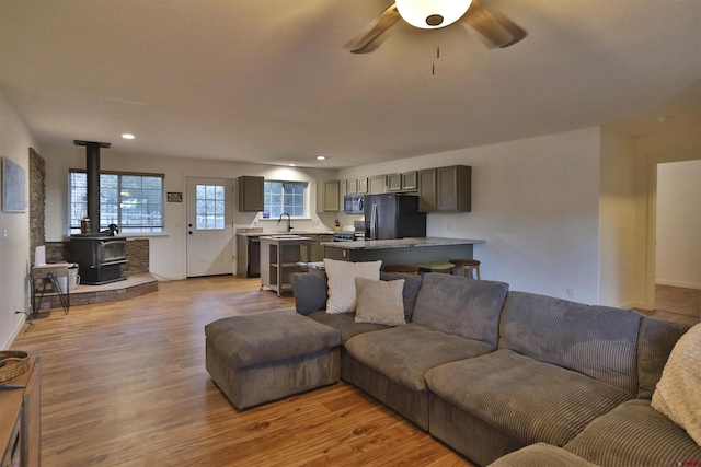 living room featuring ceiling fan, a wood stove, sink, and light wood-type flooring