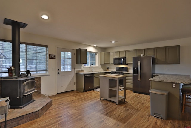 kitchen featuring a kitchen island, a breakfast bar, a wood stove, sink, and black appliances